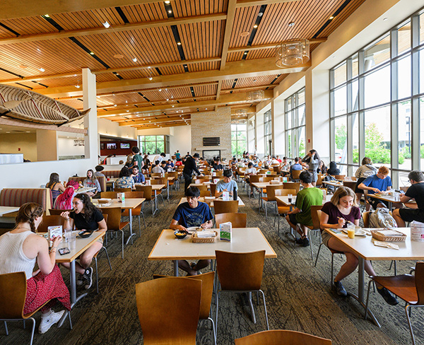 A crowded, brightly-lit dining hall filled with students eating lunch. 